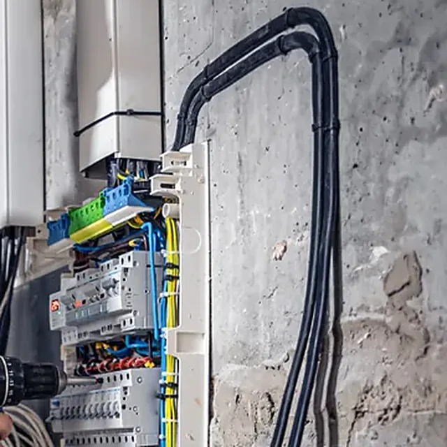 Cables negros de conductores eléctricos tendidos sobre un muro junto a un tablero
