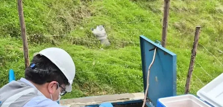 Profesional con casco tomando muestras de agua junto a una hielera