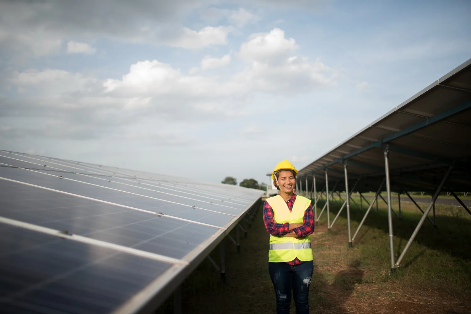 Trabajadora con chaleco reflectivo y casco amarillo junto a paneles solares